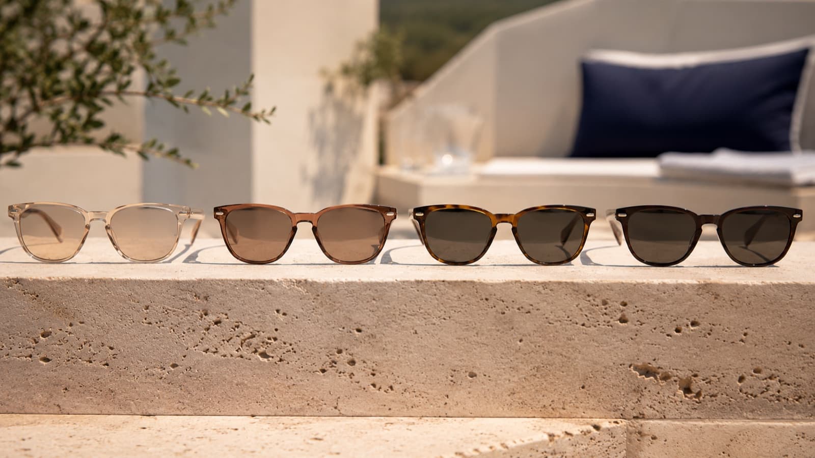 Quatre paires de lunettes de soleil alignées sur une pierre claire en plein soleil, teintes de verres du plus clair au plus foncé
