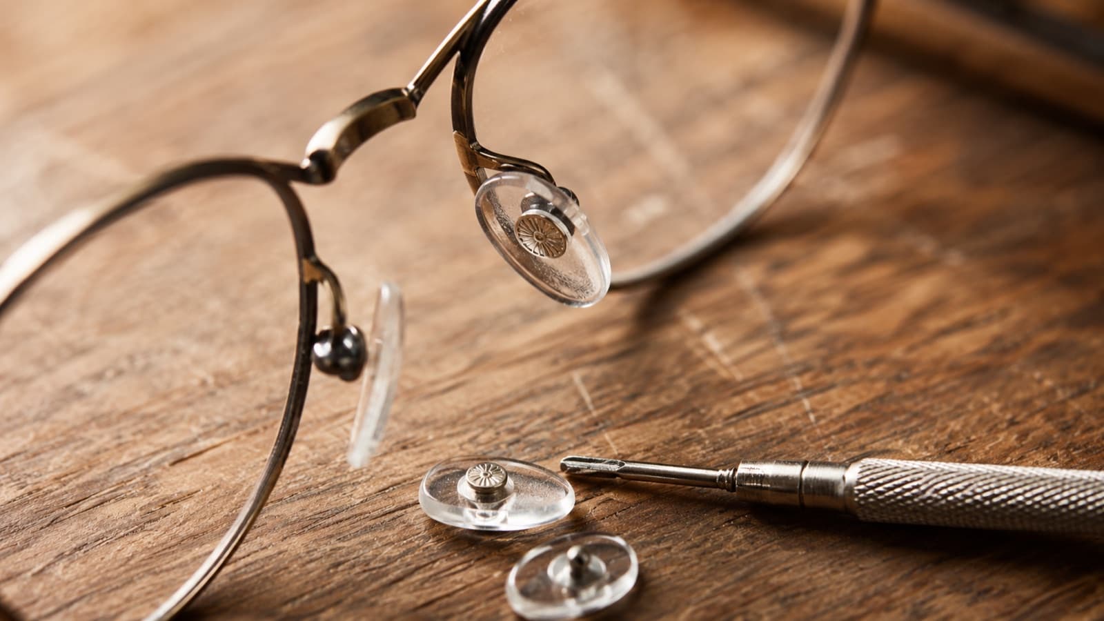 Gros plan sur les plaquettes de nez d’une monture métallique posée sur un établi d’opticien, à côté de plaquettes de rechange