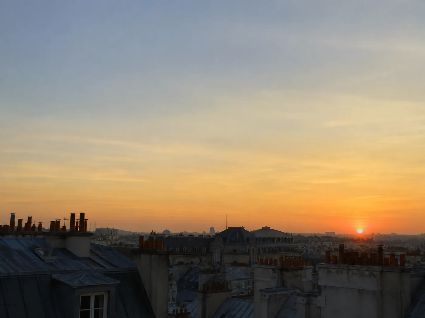 Soleil très bas au-dessus des toits en zinc de Paris en fin de soirée